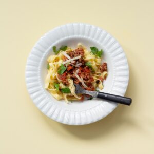 En vit tallrik med bandpasta. På pastan ligger en krämig köttfärssås.