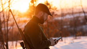 ung jägare i skogen som är snötäckt. han letar efter information i sin smartphone.